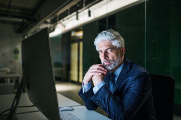 Portrait of mature businessman with computer in an office, looking at camera.