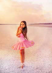 girl ballerina dancer in a pink dress on a snow-white salty dried lake. Fantastic landscape and a girl in red punata and a pink dress.