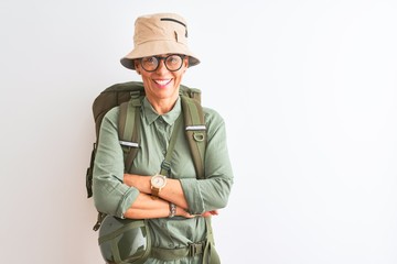 Fototapeta premium Middle age hiker woman wearing backpack canteen hat glasses over isolated white background happy face smiling with crossed arms looking at the camera. Positive person.