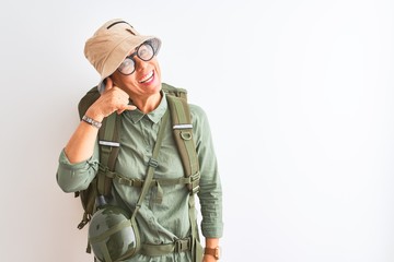 Middle age hiker woman wearing backpack canteen hat glasses over isolated white background smiling doing phone gesture with hand and fingers like talking on the telephone. Communicating concepts.