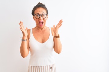 Middle age woman wearing casual t-shirt and glasses standing over isolated white background celebrating crazy and amazed for success with arms raised and open eyes screaming excited. Winner concept