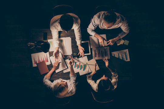 Top above high angle view of four smart clever hardworking business people executive managers preparing strategy report analysis research talking at late night workplace workstation