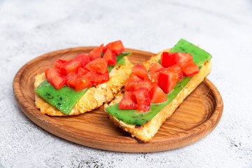 two Italian bruschettes with cheese and tomatoes on a wooden plate