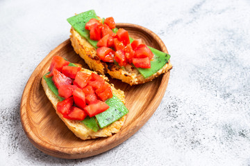 two Italian bruschettes with cheese and tomatoes on a wooden plate