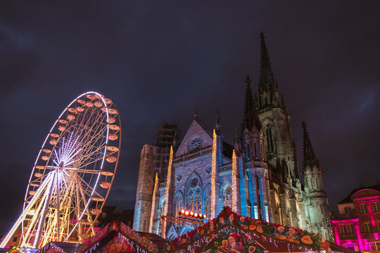 Night view of the traditional christmas market, the big wheel attraction and the illuminated Cathedral in the historic center of Mulhouse, Alsace