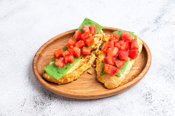 two Italian bruschettes with cheese and tomatoes on a wooden plate