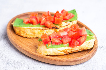 two Italian bruschettes with cheese and tomatoes on a wooden plate