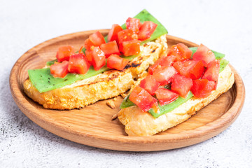 two Italian bruschettes with cheese and tomatoes on a wooden plate