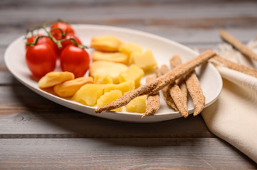 Italian food is grissini bread with prosciutto, cheese and tomatoes with herbs on a plate on a wooden background. Healthy style. Close up