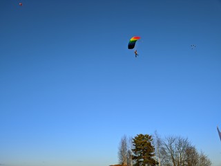 Winter Sunny landscape with landing skydiver with bright parachute on the background of forest, blue sky, snow and grass