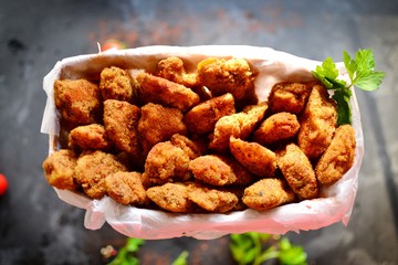 Chicken nuggets on a dark background. Grilled fish and meat in batter. Fish sticks. Meat sticks. Nuggets with tomato and parsley in a basket. Place for your text. Top view