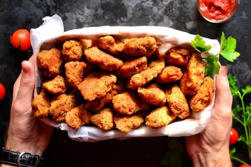 chicken nuggets with a crispy crust. hands in the frame. hands and food. a man holds a basket of...