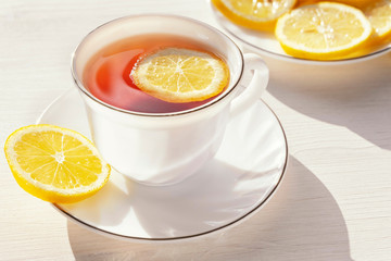 White cup with tea and slices of lemon in the morning sunlight.