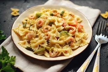 Italian pasta in a creamy sauce with shrimp on a plate, top view. Pasta in the form of bows on a dark table background. 