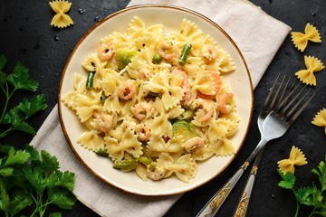 Italian pasta in a creamy sauce with shrimp on a plate, top view. Pasta in the form of bows on a dark table background. 