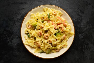 Italian pasta in a creamy sauce with shrimp on a plate, top view. Pasta in the form of bows on a dark table background. 
