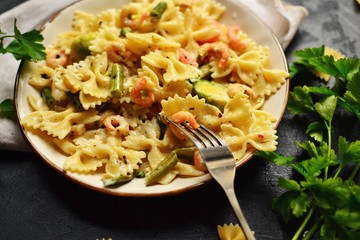Italian pasta in a creamy sauce with shrimp on a plate, top view. Pasta in the form of bows on a dark table background. Hands in the frame. The girl holds a beautiful plate with pasta food.