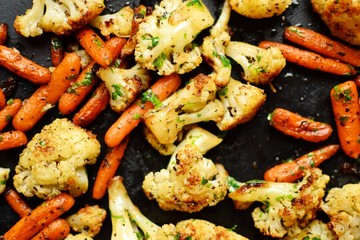 Baked cauliflower and carrot. Grilled vegetables on a dark table background. Healthy vegan food.