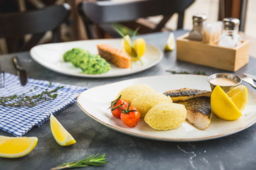 Fish dishes with millet porridge, tomatoes, lemon slice and shrimp sauce on table