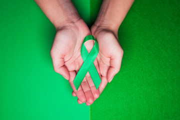 Jade tape in support of patients with hepatitis B and hepatocellular carcinoma. Green ribbon on female hands on grass background - obrazy, fototapety, plakaty