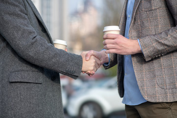 Two men with coffee cups shaking each others hand