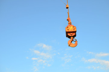 Large yellow crane hook on lifting fears and chains hanging on it for lifting loads on a background of blue sky. Construction concept - Image