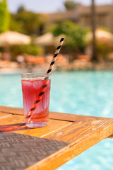 Red cocktail with ice with a straw on the background of the pool. vertical photo