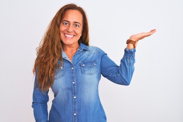 Middle age mature woman wearing denim jacket standing over white isolated background smiling cheerful presenting and pointing with palm of hand looking at the camera.