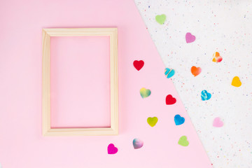Wooden frame on light pink and textile background with colorful paper hearts and dots. Valentine, wedding, card concept. Top view, flat lay, copy space, mock up