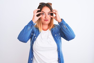 Beautiful woman wearing denim shirt standing over isolated white background Trying to open eyes with fingers, sleepy and tired for morning fatigue