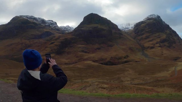 A woman on winter clothes taking pictures of the mountains in the Scotland highlands during fall