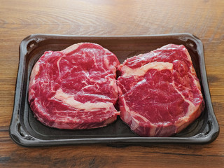 Two raw uncooked premium fresh rib eye steaks on a plastic tray, Top quailty product from supermarket. On a wooden table.