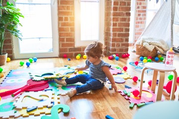 Beautiful toddler sitting on the floor playing with building blocks toy at kindergarten