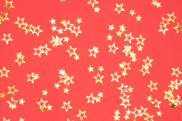 Golden stars Christmas background on bright red, flatlay, selective focus