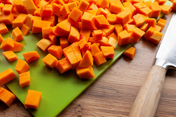 Vibrant, bright orange butternut squash, cut in cubes on green cutting board