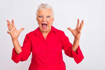 Senior grey-haired woman wearing red casual shirt standing over isolated white background shouting with crazy expression doing rock symbol with hands up. Music star. Heavy concept.