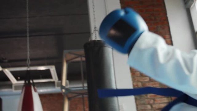 Low angle view of two young female karatekas wearing white kimono and boxing gloves training kicks and punches inside boxing ring