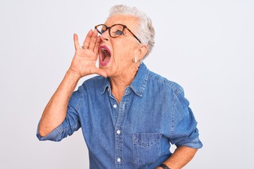 Senior grey-haired woman wearing denim shirt and glasses over isolated white background shouting and screaming loud to side with hand on mouth. Communication concept.