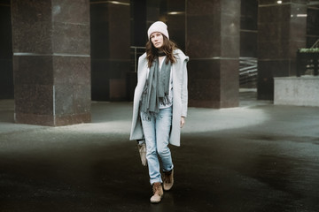 Young brunette woman walking around the city. She's wearing a gray coat and blue jeans