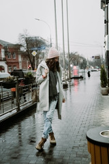 Young brunette woman walking around the city. She's wearing a gray coat and blue jeans
