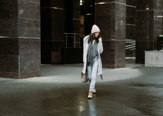 Young brunette woman walking around the city. She's wearing a gray coat and blue jeans