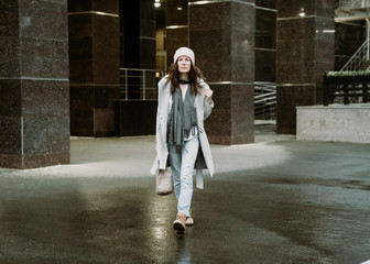 Young brunette woman walking around the city. She's wearing a gray coat and blue jeans