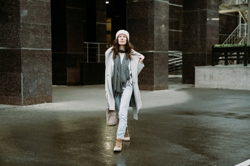 Young brunette woman walking around the city. She's wearing a gray coat and blue jeans