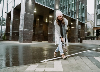Young brunette woman walking around the city. She's wearing a gray coat and blue jeans
