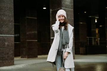 Young brunette woman walking around the city. She's wearing a gray coat and blue jeans