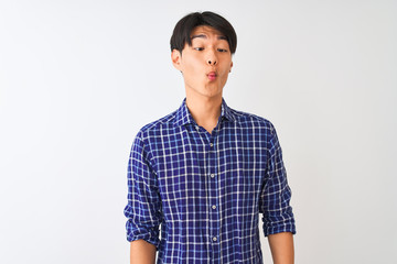 Obraz premium Young chinese man wearing casual blue shirt standing over isolated white background making fish face with lips, crazy and comical gesture. Funny expression.