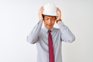 Chinese architect man wearing tie and helmet standing over isolated white background suffering from headache desperate and stressed because pain and migraine. Hands on head.