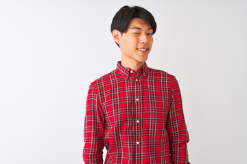 Young chinese man wearing casual red shirt standing over isolated white background winking looking at the camera with sexy expression, cheerful and happy face.
