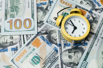 Yellow alarm clock on the stack of one hundred american dollars bills. Credit, deposit and mortgage concept.