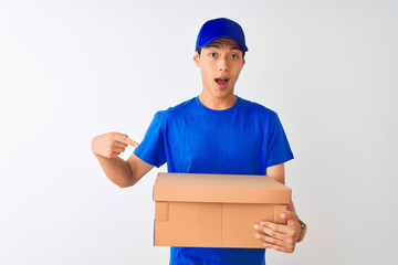 Chinese deliveryman wearing cap holding box standing over isolated white background very happy pointing with hand and finger